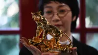 Seorang perempuan berpose dengan model harimau berlapis emas, menjelang Tahun Baru Imlek, yang ditandai sebagai Tahun Macan Air di Hanoi, pada 19 Januari 2022. Di Vietnam, perayaan Tahun Baru China disebut Tet yang merupakan salah satu perayaan paling penting masyarakat di sana. (Nhac NGUYEN/AFP)