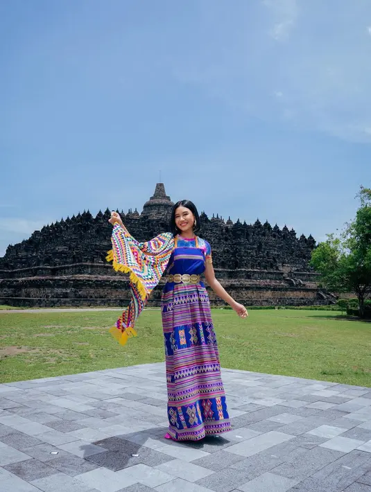 Gaun ini tampil cantik di tubuh Shenina dengan pengaplikasian belt emas. Kain bermotif warna-warni digunakan sebagai selendang yang disematkan di bahu kanan. [Instagram/shenacinnamon].