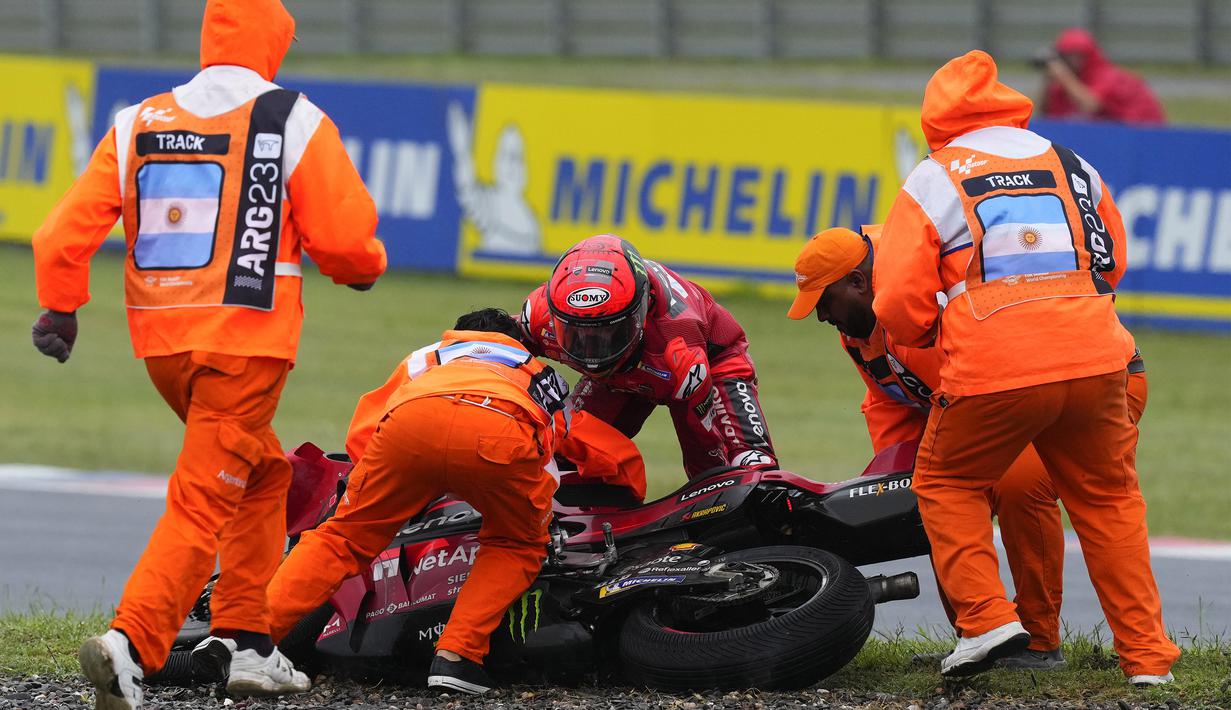 Terpleset dan tidak terlalu parah, Francesco Bagnaia berusaha mengangkat motornya dibantu beberpa orang petugas. (AP Photo/Natacha Pisarenko)