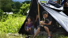 Seorang ayah memberi susu botol jus jeruk kepada putrinya yang masih bayi di tepi Sungai Huixtla, negara bagian Chiapas, Meksiko, Rabu (8/5/2022). Keluarga itu adalah rombongan dari kelompok migran, banyak dari Amerika Tengah dan Venezuela, yang meninggalkan Tapachula. (AP Photo/Marco Ugarte)