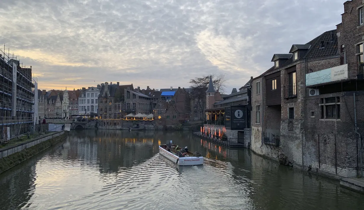 Orang-orang melakukan tur perahu melalui kanal di Ghent, Belgia, Rabu (22/12/2021). Belgia memutuskan untuk lebih memperketat pembatasan guna mengantisipasi varian Omicron yang melonjak tetapi menghindari lockdown penuh seperti yang dilakukan Belanda. (AP Photo/Virginia Mayo)