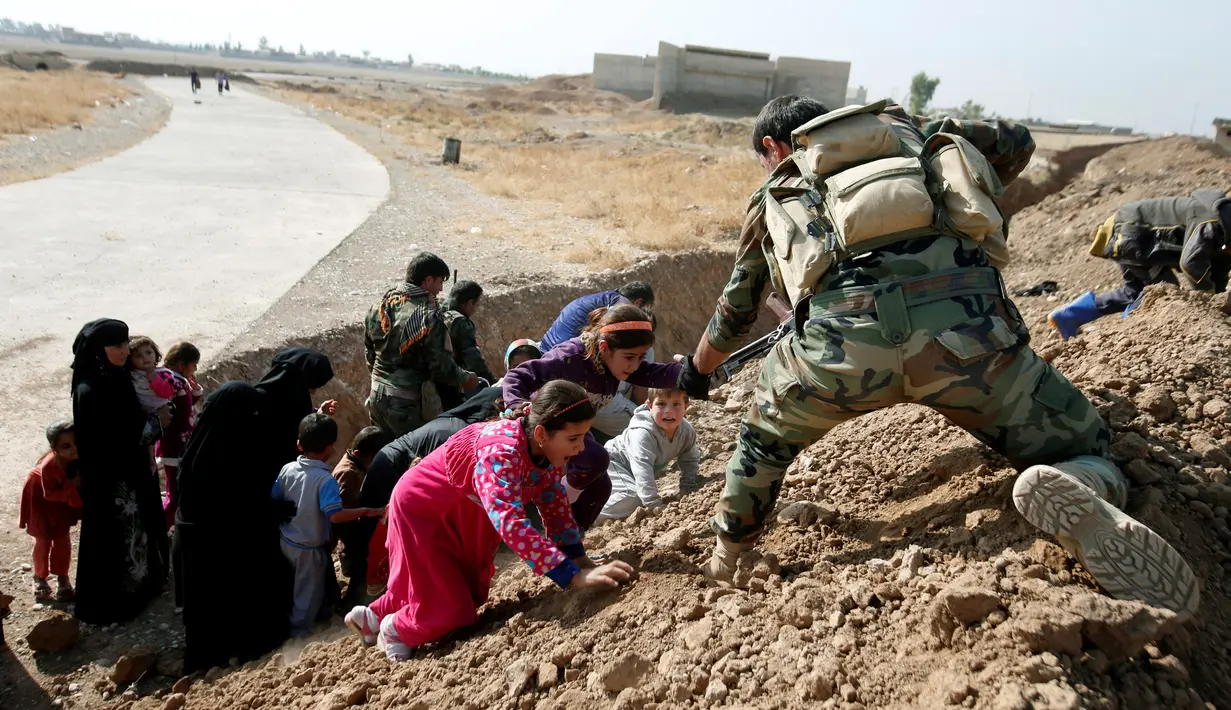 Pejuang Peshmerga Kurdi membantu perempuan dan anak-anak Irak memanjat gundukan saat melarikan diri dari desa yang dikuasai ISIS, Irak, Senin (31/10). (REUTERS / Azad Lashkari )