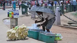 Seorang penjual makanan menggunakan payung selama musim panas di New Delhi, India (10/6/2019). Kondisi gelombang panas yang parah menyapu bagian utara dan barat India dengan suhu maksimum melonjak hingga 48 derajat Celcius ( 118 F) di beberapa bagian Rajasthan. (AP Photo/Manish Swarup)