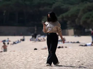 Seorang perempuan yang mengenakan masker berjalan di pantai Sa Conca di Castell-Platja D'Aro dekat Girona, Spanyol pada Rabu (31/3/2021). Spanyol memperketat aturan penggunaan masker dengan mewajibkannya di luar ruangan dan seluruh fasilitas publik. (Josep LAGO / AFP)