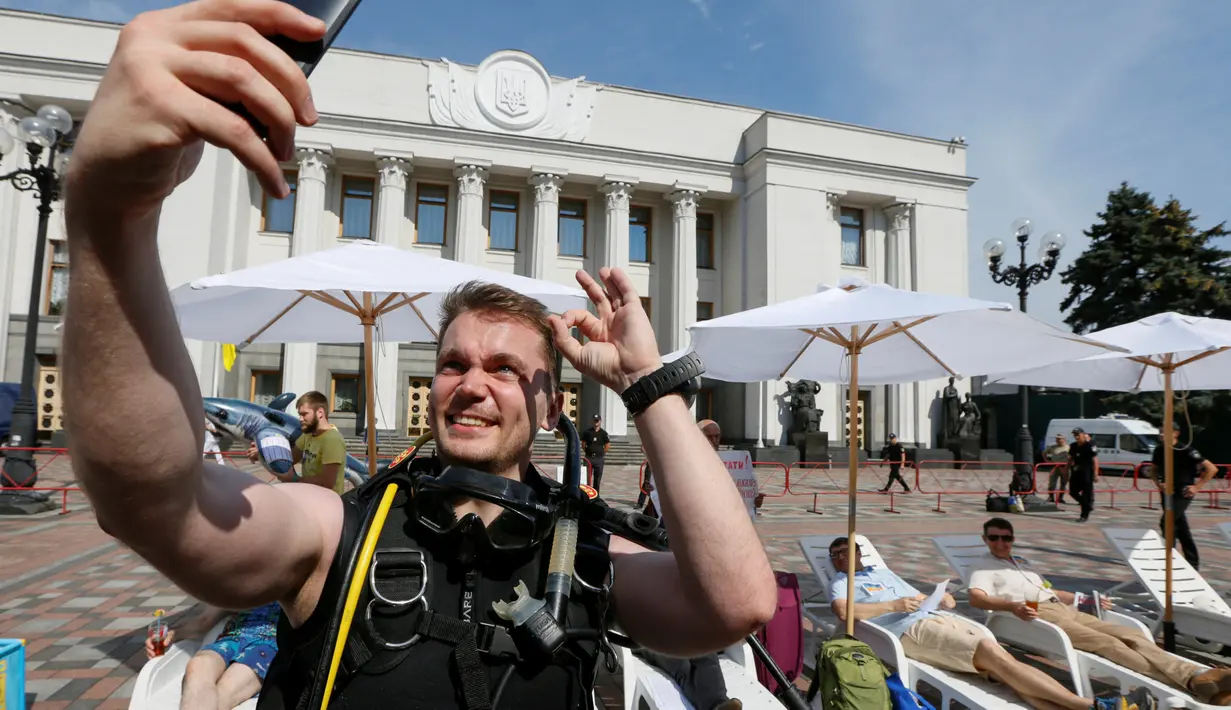 Aktivis tampak berselfie menggunakan baju menyelam di depan gedung parlemen Kiev, Ukraina, (12/7). Aksi ini mereka memprotes masa reses parlemen Kiev.( REUTERS / Valentyn Ogirenko)