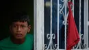 Anak laki-laki memandang ke luar jendela dengan kain merah yang menggantung untuk meminta bantuan makanan selama lockdown di Soacha, dekat Bogota, 4 April 2020. Presiden Kolombia Ivan Duque menetapkan lockdown dari 24 Maret lalu sebagai langkah mencegah penyebaran virus corona. (Raul ARBOLEDA/AFP)
