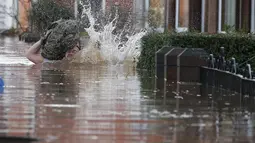 Warga tersandung saat melintasi banjir yang merendam jalan pemukiman di Carlisle, Inggris, Minggu (6/12). Puluhan ribu rumah tidak punya listrik karena Badai Desmond yang menyebabkan banjir di Inggris utara dan sebagian Skotlandia. (REUTERS/Phil Noble)