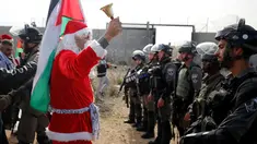 Seorang pengunjuk rasa berkostum Santa Claus menggelar aksi di desa Tepi Barat Bilin dekat Ramallah, Jumat (23/12). Mereka menentang pembangunan tembok pembatas di Israel. (REUTERS/Mohamad Torokman)