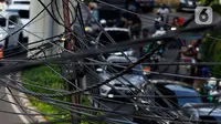 Kendaraan melintas di bawah kabel listrik dan kabel optik yang terlihat semrawut di kawasan Taman Puring, Jakarta, Jumat (3/7/2020). Kesemrawutan kabel ini sering terlihat di sejumlah kawasan Jakarta yang menyebabkan pemandangan kurang enak untuk dilihat. (Liputan6.com/Johan Tallo)