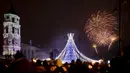 Kembang api menerangi langit di atas pohon Natal yang menyala di Lapangan Katedral di Vilnius, Lithuania selama perayaan Tahun Baru, Rabu (1/1/2020). (AP Photo/Mindaugas Kulbis)