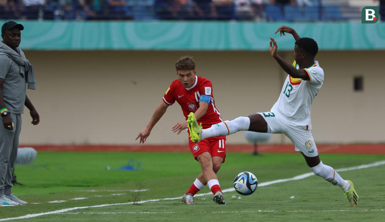 <p>Pemain Timnas Polandia U-17, Krzysztof Kolanko (kiri) melepaskan umpan yang berusaha dipotong pemain Timnas Senegal U-17, Alpha Toure pada laga kedua Grup D Piala Dunia U-17 2023 di Stadion Si Jalak Harupat, Kabupaten Bandung, Selasa (14/11/2023). (Bola.com/Ikhwan Yanuar)</p>
