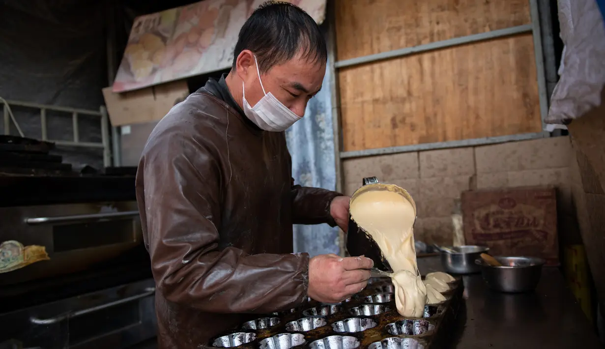 Seorang pedagang menuangkan adonan ke dalam cetakan kue di pasar di Beijing (20/11). (AFP Photo/Nicolas Asfouri)