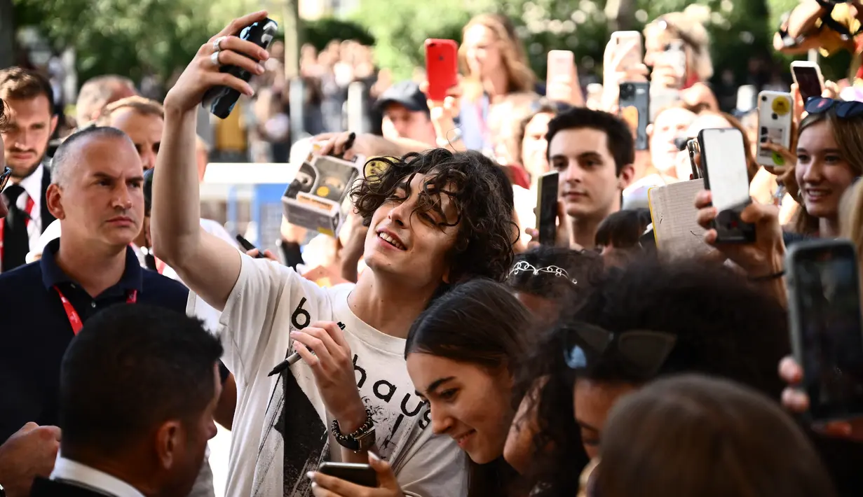 Aktor Prancis-AS, Timothee Chalamet berfoto selfie dengan penggemar saat ia tiba pada Venice Film Festival 2022 ke-79 di dermaga Hotel Excelsior di Lido, Venesia, Italia (2/9/2022). Aktor berusia 26 tahun itu menarik perhatian para penggemarnya dengan penampilannya memakai atas T-shirt putih dengan motif abu-abu. (AFP/Marco Bertorello)