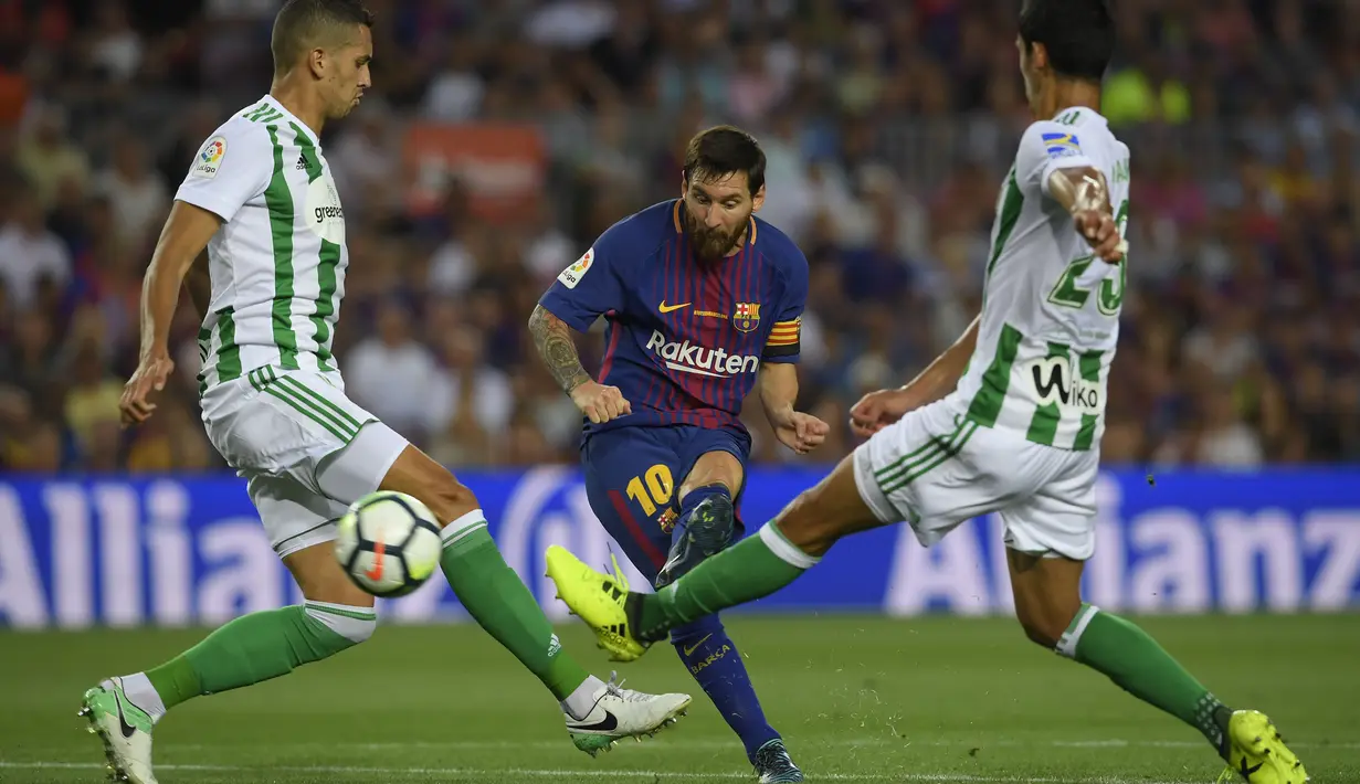 Aksi Lionel Messi (tengah) melepaskan tembakan melewati adangan dua pemain Real Betis pada lanjutan La Liga Spanyol di Camp Nou stadium, Barcelona, (20/8/2017). (AFP/Lluis Gene)