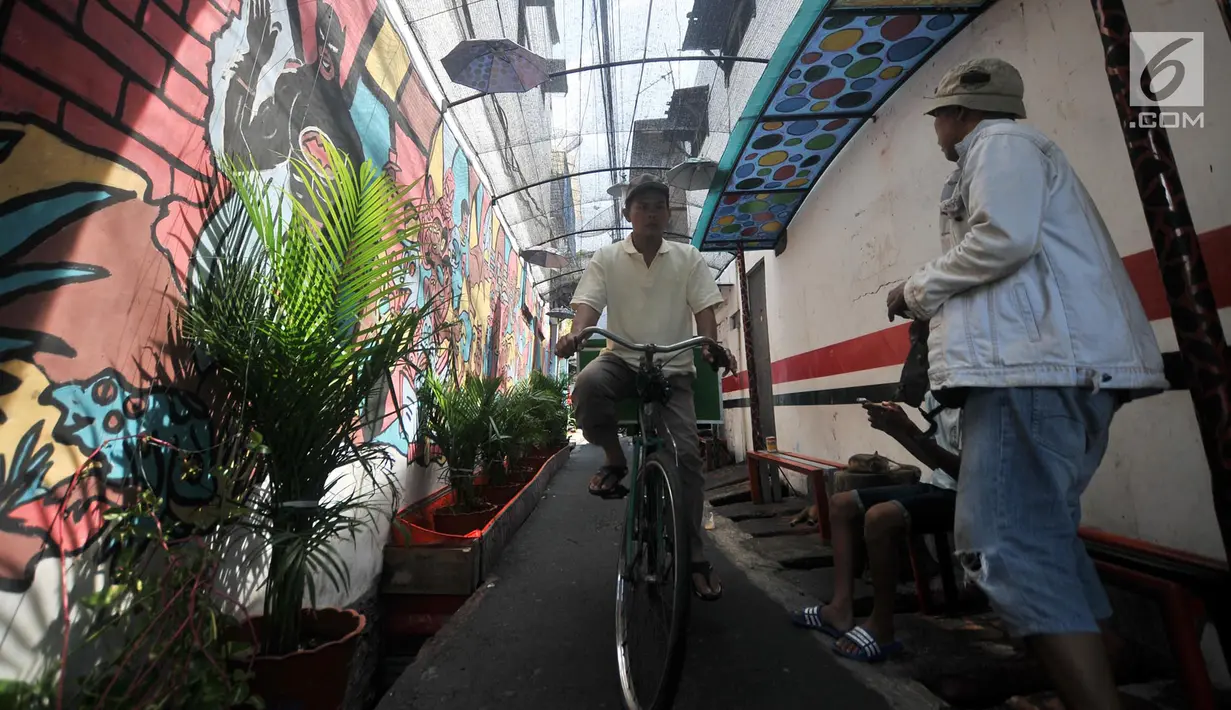 Pengendara sepeda melintas di depan lukisan tembok atau mural yang menghiasi gang di RT 13 RW 06, Jembatan Lima, Jakarta, Kamis (10/1). Warna-warni mural di pemukiman padat penduduk itu merupakan ide Aryanto selaku Ketua RT 13. (Merdeka.com/Iqbal Nugroho)