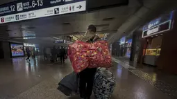 Seorang pekerja migran yang mengenakan masker membawa barang miliknya saat tiba di Stasiun Kereta Api Barat di Beijing, Jumat (6/1/2023). China berupaya meminimalkan kemungkinan wabah COVID-19 yang lebih besar selama kesibukan perjalanan Tahun Baru Imlek bulan ini menyusul berakhirnya sebagian besar langkah-langkah pencegahan pandemi. (AP Photo/Wayne Zhang)