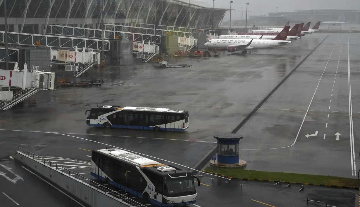 Bus dan pesawat diparkir di landasan setelah semua penerbangan dibatalkan di Bandara Internasional Pudong di Shanghai, China (25/7/2021). Topan In-fa diperkirakan akan bergerak ke utara-barat laut China dan masuk hingga ke pedalaman. (AP Photo/Andy Wong)