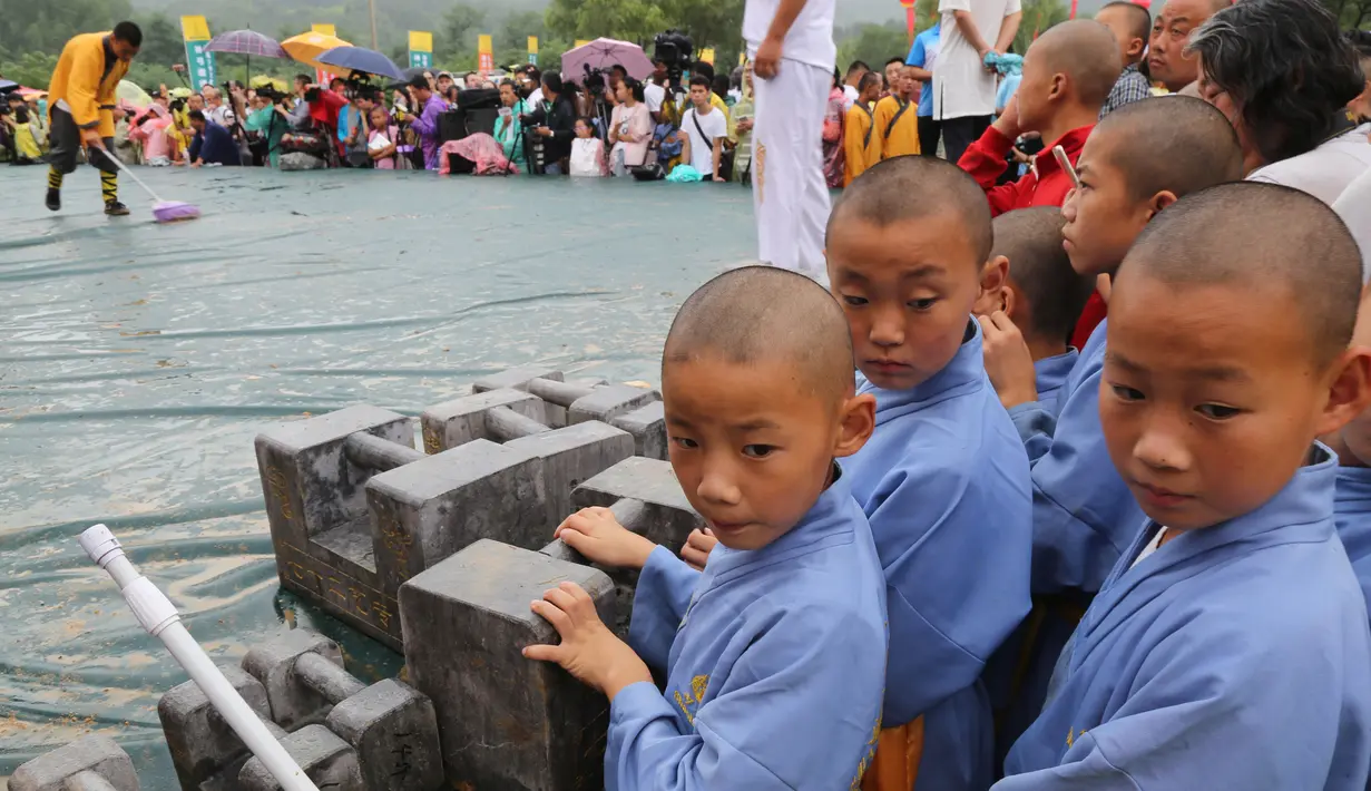 Biksu muda Shaolin berdiri di samping kunci batu saat menyaksikan kompetisi seni bela diri '72 Arts of Shaolin' di kuil Shaolin, Provinsi Henan, China, 30 Juli 2017. Kompetisi ini menampilkan para jago kungfu yang memamerkan kekuatan fisik. (STR AFP)