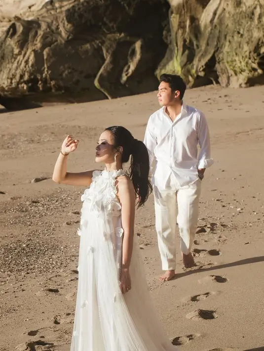 Erwin, sang kekasih, tampil dengan gaya minimalis namun tetap stylish. Mengenakan kemeja putih yang digulung ringan di bagian lengan, dipadukan dengan celana panjang putih, ia menciptakan tampilan kasual yang serasi dengan latar belakang pantai berpasir dan tebing bebatuan yang megah. [@jessicajane].