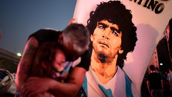 Fans legenda sepak bola Argentina Diego Maradona seorang ayah dan putrinya berduka saat mereka berkumpul untuk memberi penghormatan pada hari kematiannya di Obelisk, Buenos Aires, Argentina, 25 November 2020. (RONALDO SCHEMIDT/AFP)