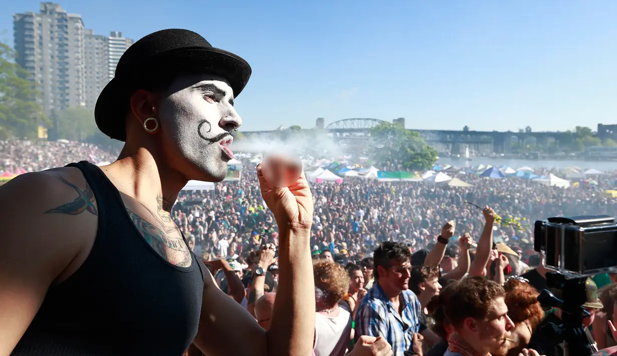 Seorang pria merokok ganja saat ribuan orang berkumpul merayakan acara legalisasi ganja 4/20 di Sunset Beach, Vancouver, Kanada (20/4). Kanada sudah menawarkan dukungan terhadap ganja untuk penggunaan medis. (AFP/Jeff Vinnick)
