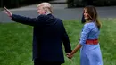 Presiden AS Donald Trump menggandeng tangan istrinya, Melania pada acara piknik merayakan Hari Kemerdekaan di halaman Gedung Putih, Rabu (4/7). Pasangan yang jarang bergandengan tangan di depan umum itu langsung mencuri perhatian. (AFP/Brendan Smialowski)