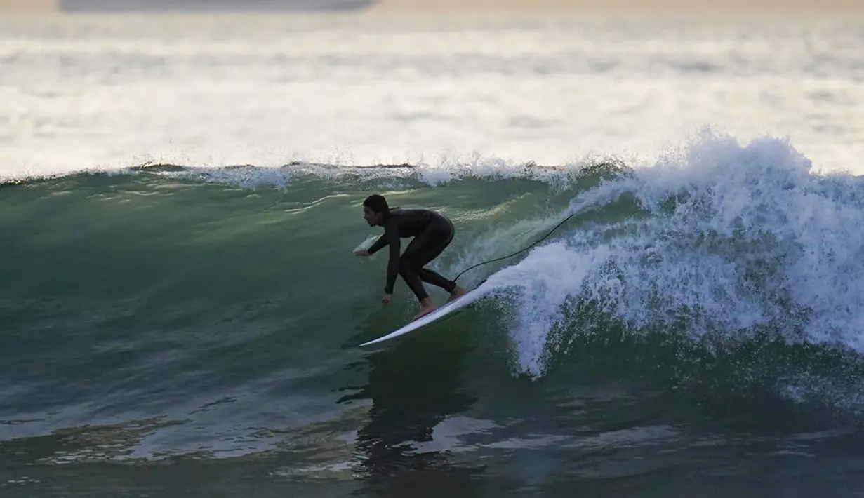 Seorang peselancar mengendarai ombak di Huntington Beach, California, Amerika Serikat, 12 Januari 2022. Peselancar di seluruh California Selatan berbondong-bondong ke daerah pantai saat gelombang ombak besar memasuki wilayah tersebut. (AP Photo/Ashley Landis)