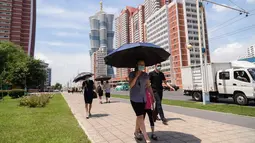 Orang-orang berlindung di bawah payung saat mereka berjalan di sepanjang Mirae Street selama suhu 34 derajat celsius, di Pyongyang, Korea Utara, Rabu (21/7/2021). Musim Panas dimulai pada bulan Juni hingga Agustus, dan puncak musim panas adalah bulan Agustus. (KIM Won Jin / AFP)