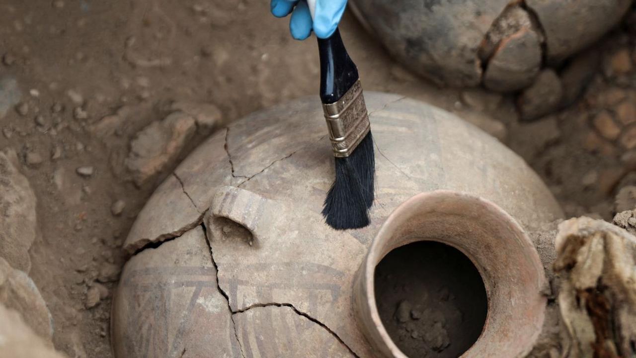 Seorang arkeolog membersihkan benda bejana keramik yang ditemukan di samping mumi berusia 1.000 tahun di situs arkeologi di lingkungan perumahan, di Lima, Peru (6/9/2023).