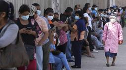 Seorang wanita mengenakan masker dan face shield melewati antrean orang yang menunggu tes PCR di Lima, Rabu (5/1/2022).Peru mengonfirmasi pada Selasa dimulainya gelombang ketiga infeksi virus corona di mana negara itu mencatat 309 kasus varian omicron yang sangat menular. (AP Photo/Martin Mejia)
