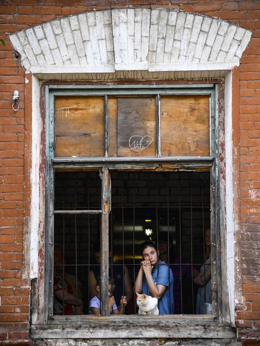 Seorang wanita melihat keluar jendela dari asrama para pekerja pabrik tekstil Proletarka di Kota Tver, Rusia, 8 Agustus 2020. Kota Tver yang unik serta padat dilupakan oleh otoritas baru dan diubah menjadi ghetto miskin yang kotor. (Alexander NEMENOV/AFP)