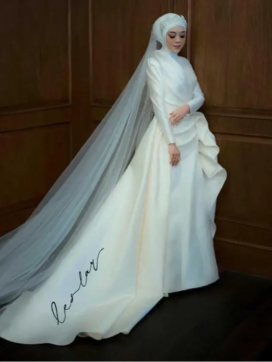 Lesti Kejora memilih mengenakan gaun pernikahan dari Hian Tjen dengan dengan gaun satun bertulisan singkatan nama dirinya dan suami. Ia pun menawan dengan hijab dihiasi mahkota dan veil menyapu lantai. [@lestykejora]
