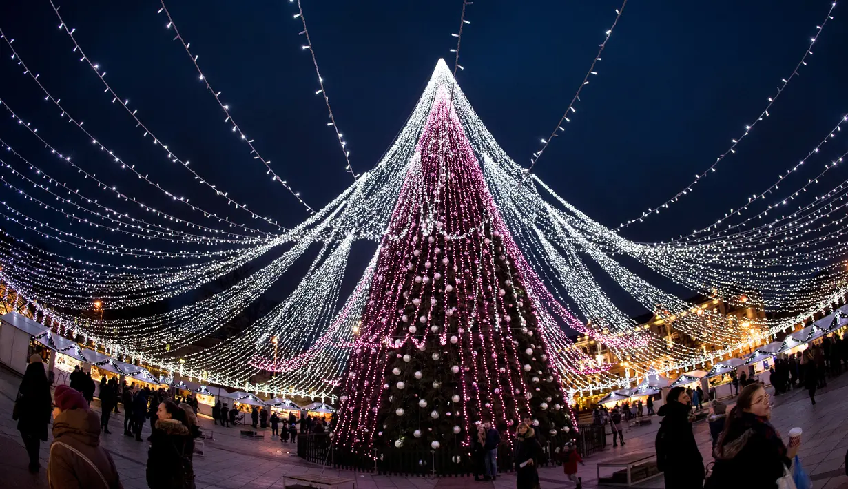 Pengunjung berjalan di sekitar pohon Natal raksasa yang menerangi Alun-Alun Katedral di Vilnius, Lithuania, 5 Desember 2017. Di sisi lain, pohon Natal tampak seperti bintang raksasa yang ada di bumi jika dilihat dari ketinggian (AP Photo/Mindaugas Kulbis)