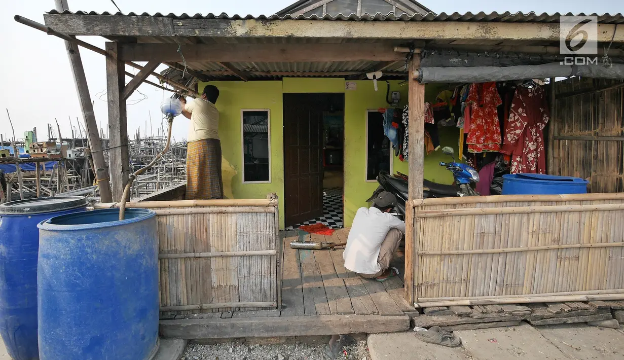 Warga memperbaiki talang yang menyalurkan air ke dalam tong di rumahnya, Kampung Kamal Muara, Jakarta, Selasa (9/7/2019). Sebagian besar warga Kampung Kamal Muara memasang pipa pada talang air di tepi atap rumah mereka untuk menampung air hujan. (Liputan6.com/Herman Zakharia)
