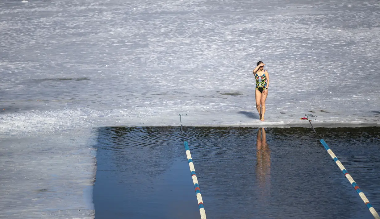 Seorang perempuan bersiap berlaga di kompetisi renang musim dingin di lubang es sepanjang 25 meter di sebuah danau dekat Vilnius, Lithuania, Sabtu (6/3/2021).  Suhu air saat itu 3 derajat Celcius, sedangkan udaranya -3 derajat Celsius. (AP Photo/Mindaugas Kulbis)