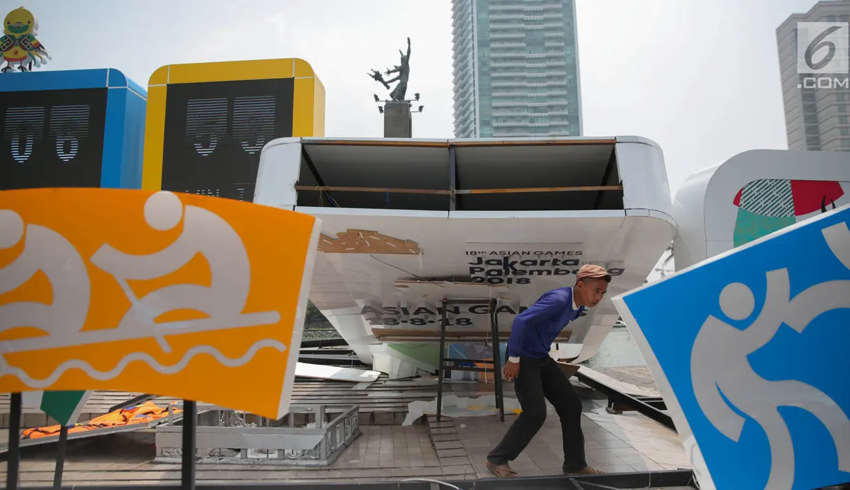 Pekerja melintas dibawah papan sosialisasi Asian Games 2018 terlihat roboh akibat hujan angin di Bundaran HI, Jakarta, Senin (11/9). (Liputan6.com/Faizal Fanani)