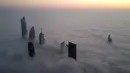 Foto udara memperlihatkan pemandangan gedung pencakar langit di tengah kabut tebal, Kuwait City, 21 Januari 2023. Kuwait memiliki gedung-gedung pencakar langit yang bahkan sampai menembus awan. (YASSER AL-ZAYYAT/AFP)