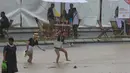 Penonton melintasi area banjir saat hujan lebat yang menyebabkan penundaan Race 1 World Superbike (WSBK) di Pertamina Mandalika International Street Circuit, Lombok Tengah, Nusa Tenggara Barat, Sabtu (20/11/2021). Hujan deras memaksa Race 1 WSBK Mandalika ditunda pada 21 November. (BAY ISMOYO/AFP)