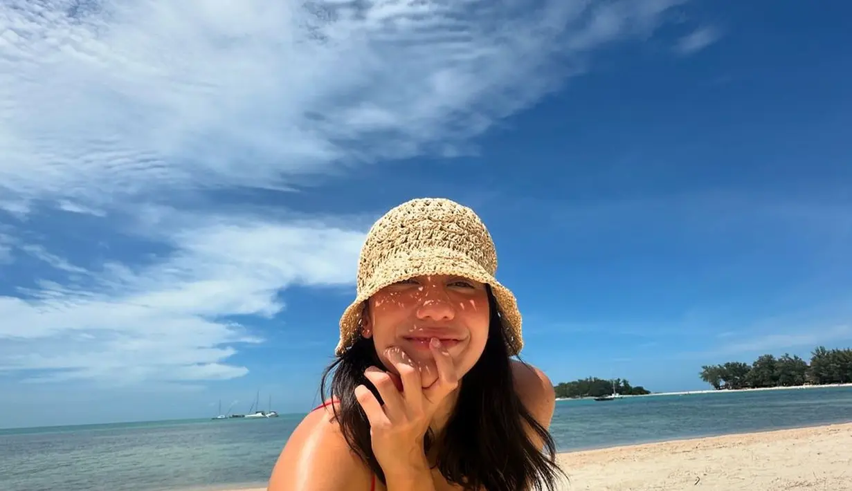 Cantiknya Pevita pakai swimsuit merah dan topi dari jerami berjemur di bawah langit biru di pinggir pantai. [Foto: Instagram/pevpearce]