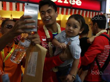 Tontowi Ahmad menggendong anak dan menlayan foto bersama fans saat tiba di Bandara Soekarno-Hatta, Cengkareng (29/8/2017). Tontowi/Liliyana meraih medali emas pada kejuaraan dunia di Glasgow. (Bola.com/Nicklas Hanoatubun)