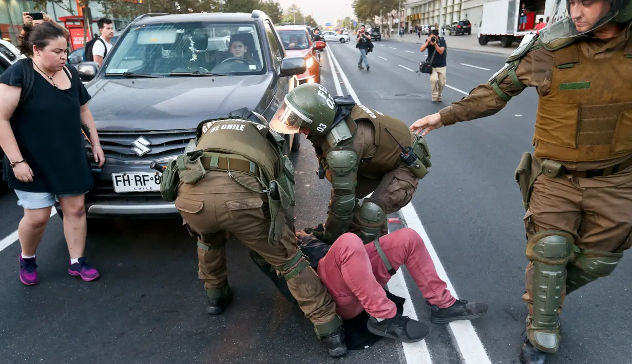 Seorang pengunjuk rasa ditahan oleh polisi anti huru hara saat demonstrasi di luar kedutaan AS di Santiago, Chili (14/4). Para demonstran melakukan aksi menentang serangan AS dan sekutunya ke Suriah. (AP / Esteban Felix)