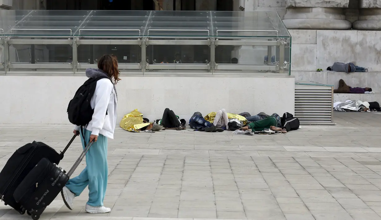 Seorang wanita berjalan di dekat sejumlah imigran yang tidur di luar stasiun kereta api Milan, Jumat (12/6/2015). (REUTERS/Stefano Rellandini)