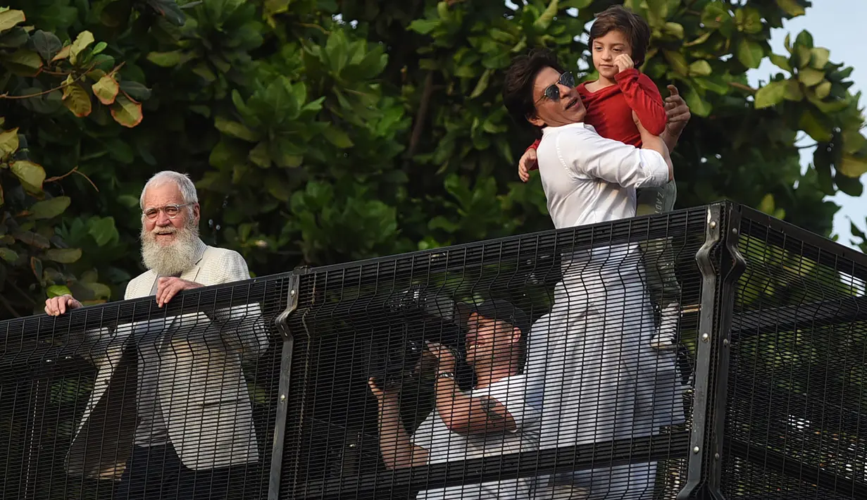 Aktor Bollywood, Shah Rukh Khan menggendong putranya, Abram Khan menyapa para fans yang berkumpul di depan rumahnya pada perayaan Idul Fitri di Mumbai, Rabu (5/6/2019). Ribuan penggemar kerap berkumpul di depan rumah Shah Rukh Khan di momen-momen tertentu. (SUJIT JAISWAL/AFP)