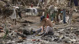 Seorang pria mencuci pakaiannya di sungai dekat puing-puing yang tersisa setelah air banjir meluluhlantahkan desa Nanxinfang di pinggiran Beijing, Jumat, 4 Agustus 2023. (AP Photo/Ng Han Guan)