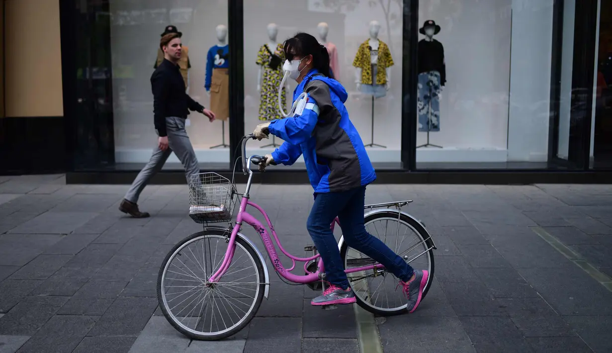 Seorang wanita mengenakan masker mengendarai sepedanya melewati sebuah toko di Beijing (19/4). Beijing memiliki populasi 21.150.000 pada tahun 2013. (AFP Photo/Wang Zhao)