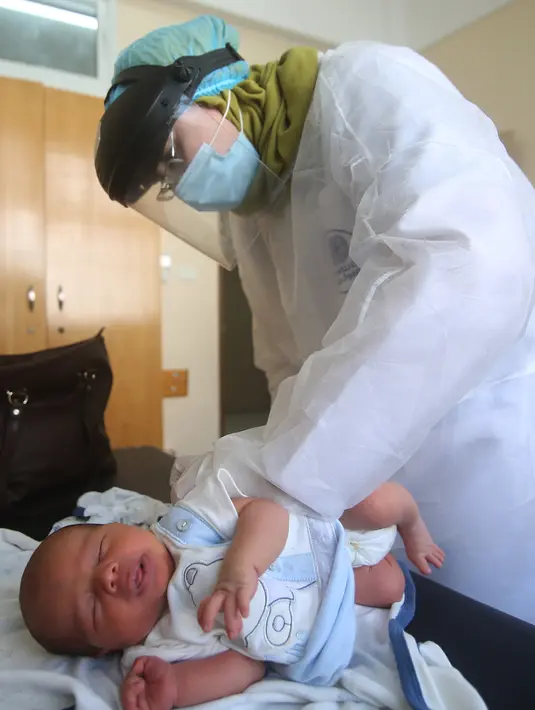 Seorang petugas medis yang mengenakan alat pelindung diri memeriksa seorang bayi di sebuah pusat layanan kesehatan saat pemberlakuan lockdown, Kota Rafah, Jalur Gaza, 9 September 2020. (Xinhua/Khaled Omar)