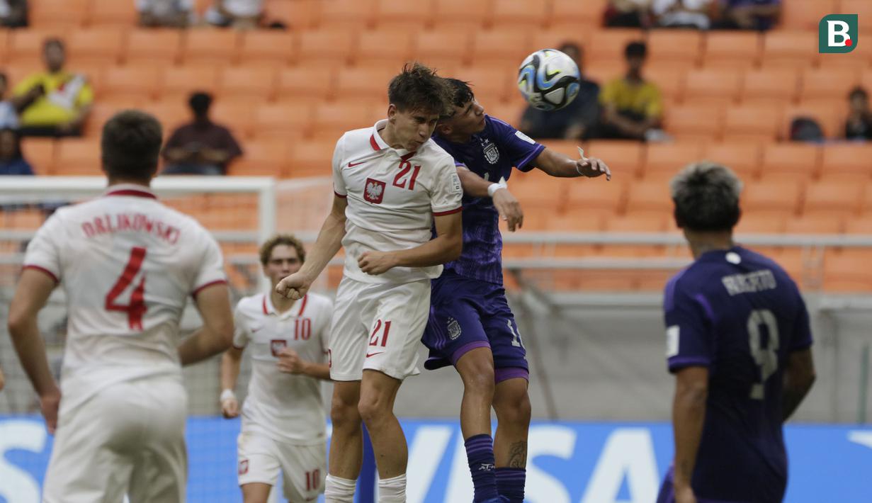 <p>Pemain Timnas Polandia U-17, Marcel Regula (tengah kiri) berduel udara dengan pemain Timnas Argentina U-17, Thiago Laplace pada laga ketiga Grup D Piala Dunia U-17 2023 di Jakarta International Stadium (JIS), Jakarta Utara, Jumat (17/11/2023). (Bola.com/Ikhwan Yanuar)</p>