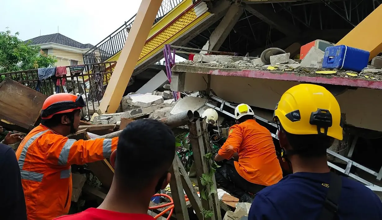 Tim penyelamat mencari korban yang terperangkap dalam sebuah bangunan runtuh di Mamuju, Sulawesi Barat, Indonesia, Jumat (15/1/2021). BMKG menyebut pusat gempa berada di darat, 6 kilometer timur laut Majene pada kedalaman 10 kilometer. (HANDOUT/NATIONAL SEARCH AND RESCUE AGENCY/AFP)