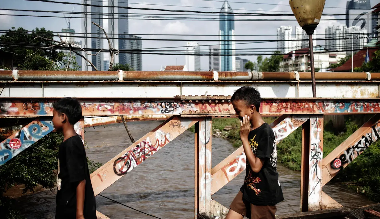 Anak anak melintasi jembatan dari kayu yang menjadi penghubung antara Jalan Karet Pasar Baru VII, Karet Tengsin dan Jalan Pam Baru, Bendungan Hilir, Tanah Abang, Rabu (30/1). (Liputan6.com/Faizal Fanani)