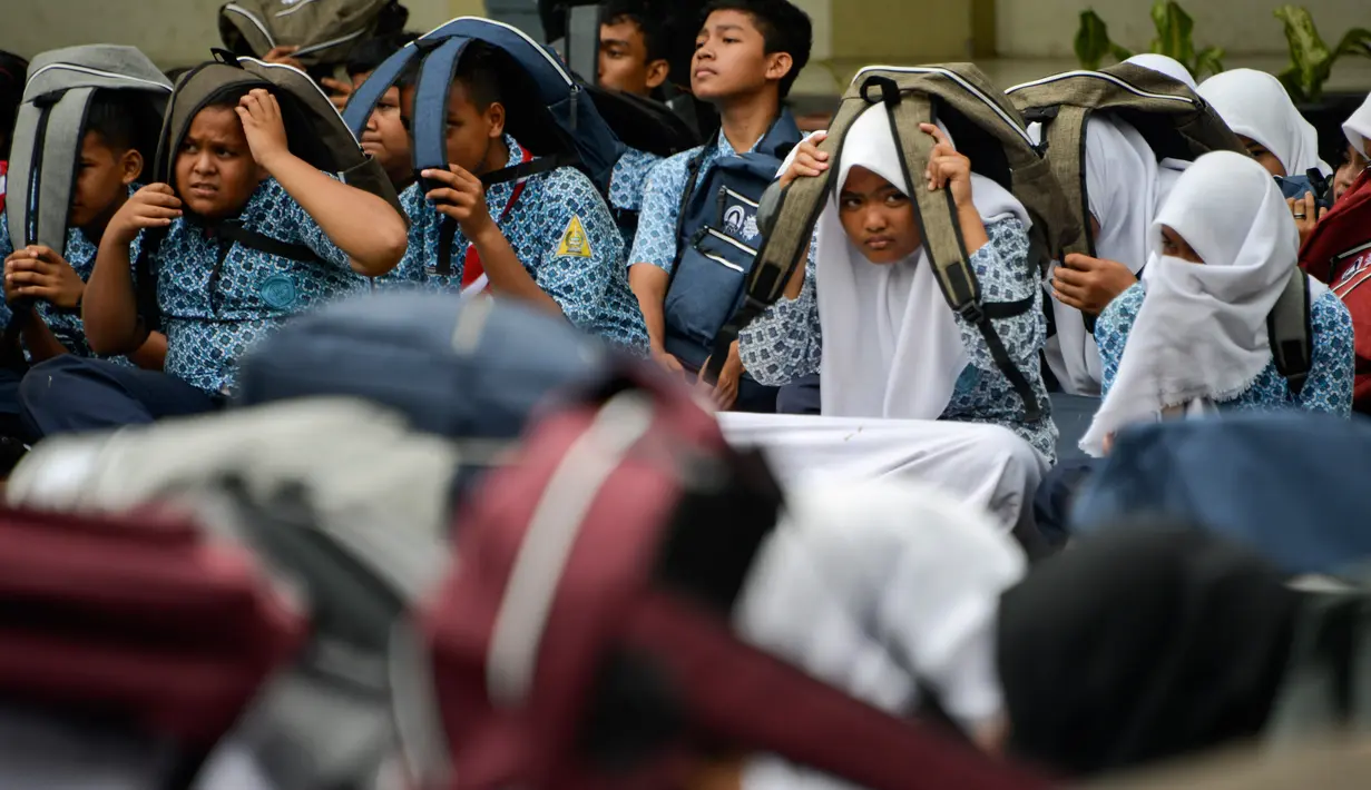 Siswa berlari ke lapangan dengan melindungi kepalanya saat simulasi bencana gempa dan tsunami di sebuah sekolah di Banda Aceh, Aceh, Rabu (9/10/2019). Simulasi dilakukan karena Aceh merupakan daerah rawan kedua bencana tersebut dan turut merusak bangunan sekolah. (Photo by CHAIDEER MAHYUDDIN / AFP)